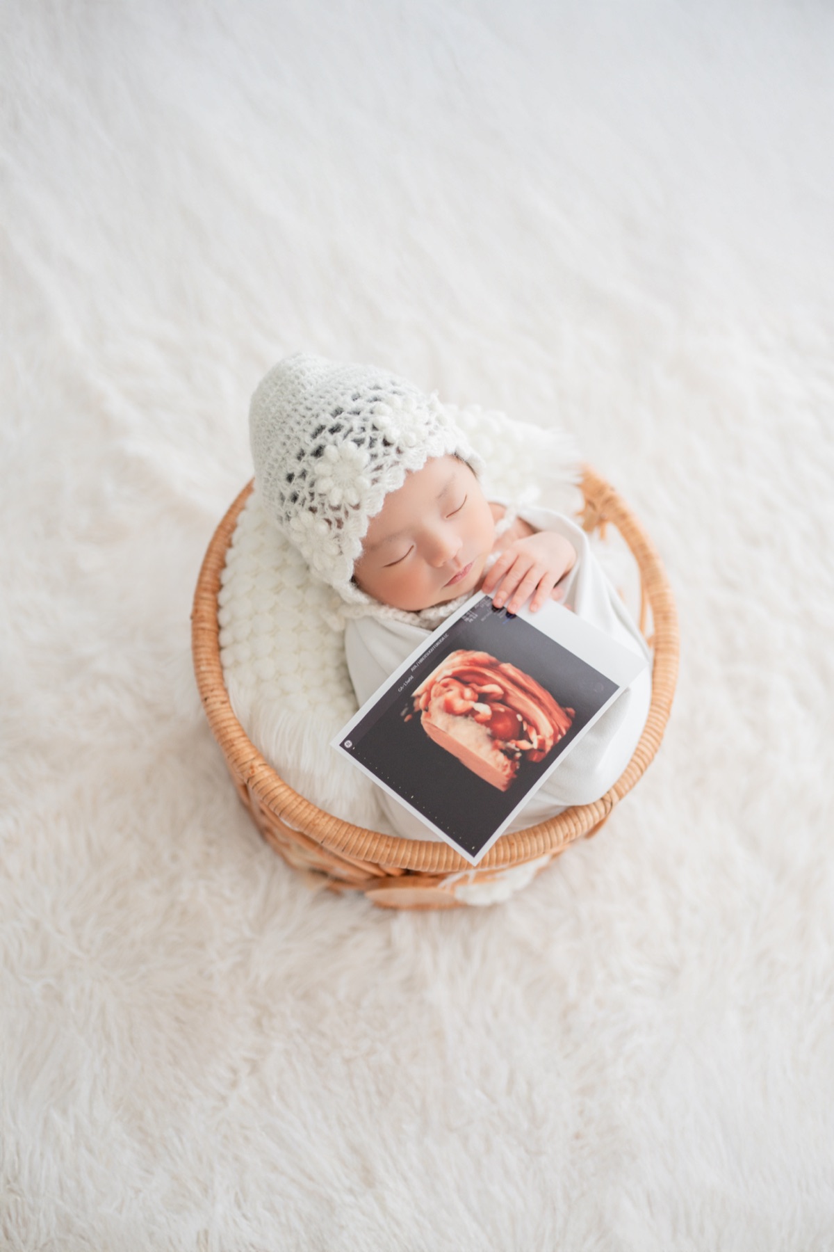 エコー写真と一緒にかごで眠る新生児
