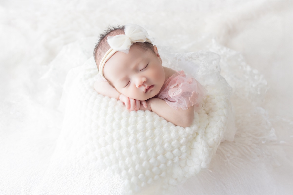 ピンクのリボンをつけて白いニットの上で眠る赤ちゃん