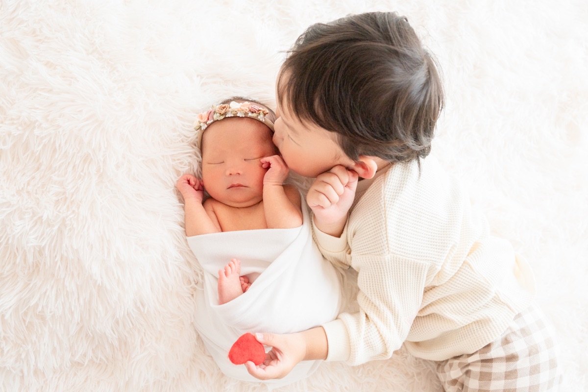 眠る新生児にそっとキスするおにいちゃん