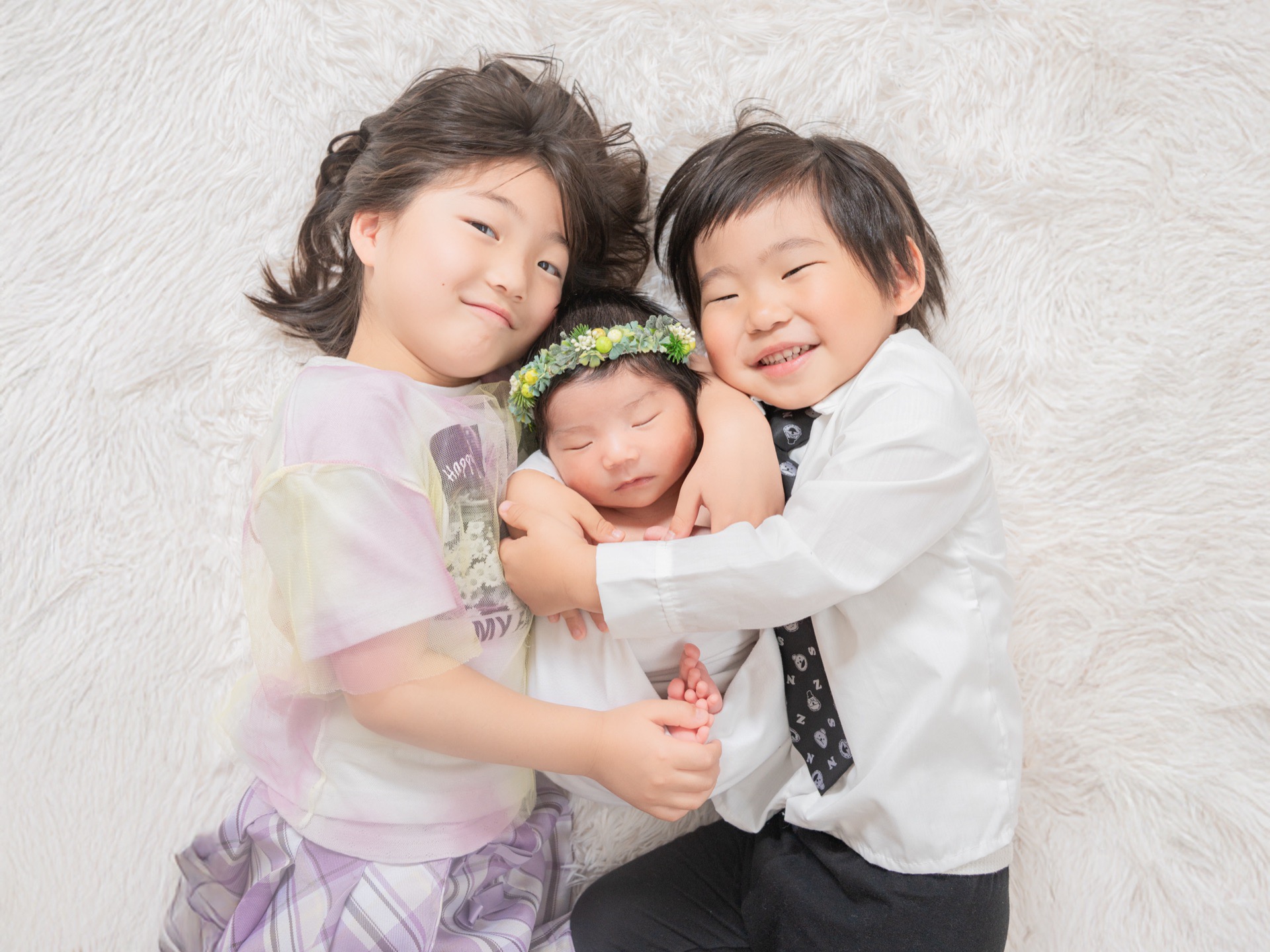 赤ちゃんを真ん中にきょうだいで寄り添う記念写真